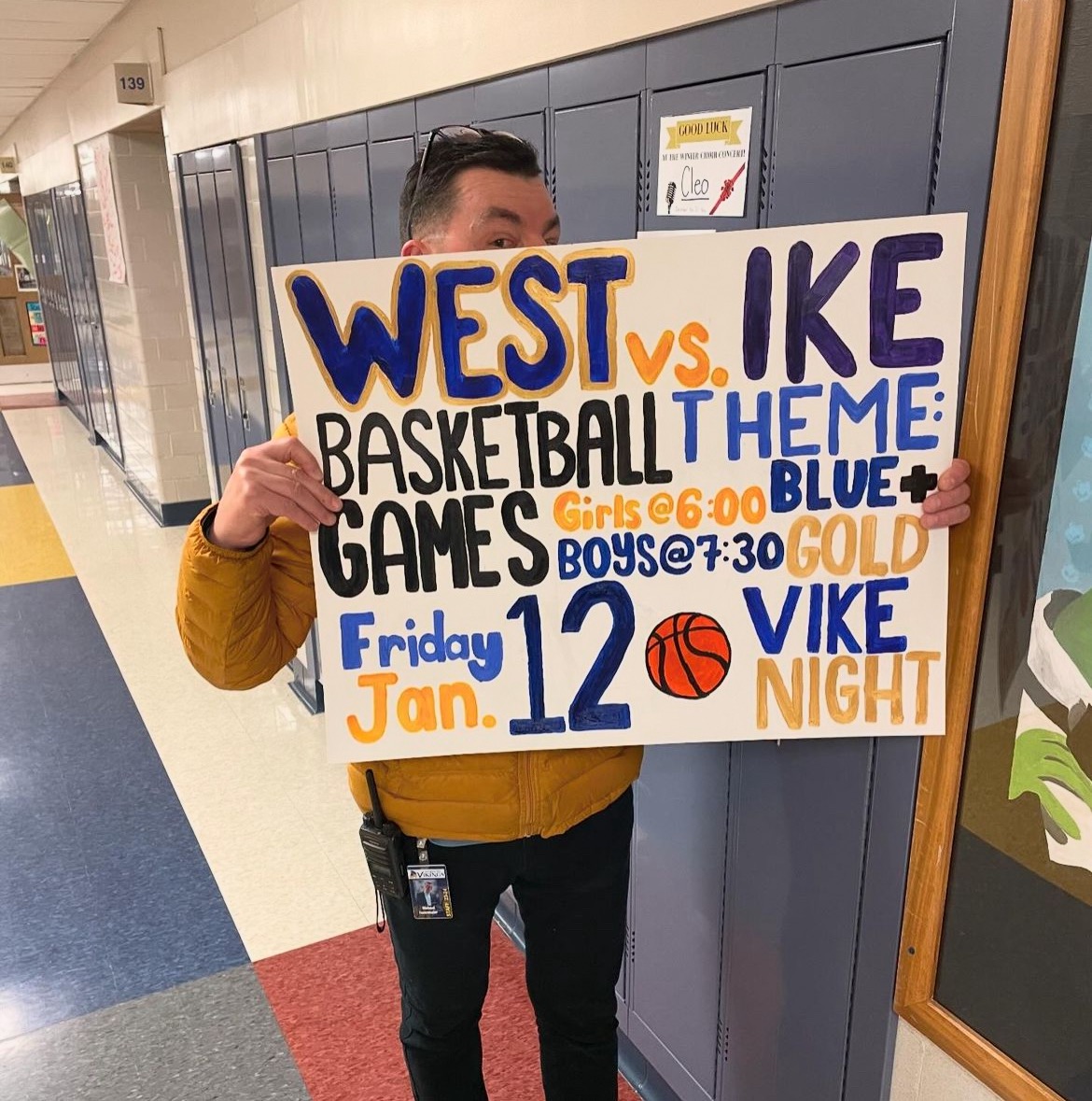 Principal Michael Fesenmaier holds an West vs Ike Basketball poster for Fridays Vike Night!